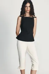 Pantalón capri de tiro alto en color crudo, con detalle de lazos ajustables en los bajos y cierre lateral con cremallera oculta.