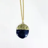 Collar con cadena de eslabones dorados y dije de piedra semipreciosa, posiblemente ágata, de forma semicircular. La parte superior del dije tiene un acabado metálico dorado martillado, mientras que la inferior es de piedra azul oscuro con vetas.