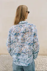 Camisa de manga larga con cuello solapa y cierre frontal de botones, confeccionada en tejido combinado semitransparente con estampado floral en tonos azules y blancos.