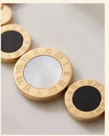Pulsera de acero con baño de oro, compuesta por una cadena de eslabones y tres dijes circulares centrales, uno de nácar blanco y dos de ónix negro.