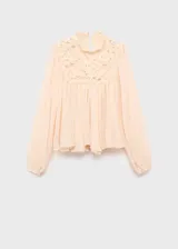 Blusa de gasa color beige claro, con cuello redondo, mangas largas abullonadas, panel frontal superior de encaje y diseño evasé con volados en el ruedo.