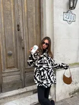 Buzo de peluche con estampado animal print en blanco y negro, de corte holgado, cuello alto y cierre frontal parcial con tirador metálico.