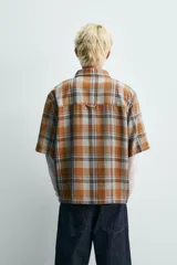 Camisa de corte boxy fit confeccionada en tejido de algodón, con estampado de cuadros en tonos tierra. Presenta cuello solapa, manga corta y cierre frontal de botones.