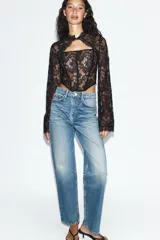 Top de encaje negro con cuello alto, mangas largas acampanadas, corsé interior estructurado y bajo asimétrico.