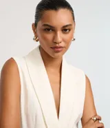 Chaleco sastre alargado color blanco hueso con finas rayas verticales. Presenta cuello tipo blazer, cierre cruzado con un botón metalizado y un lazo ancho para ajustar a la cintura.