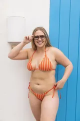 Conjunto de bikini de lycra color naranja con rayas verticales blancas. El corpiño es de corte triangular con tirantes finos y la bombacha es tipo colaless con tiras laterales ajustables.