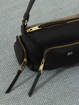 Bandolera de cuero vacuno color negro, con forma rectangular y correa ajustable para llevar al hombro o cruzada. Presenta múltiples bolsillos exteriores con cierre y un bolsillo frontal con cierre y logo grabado.