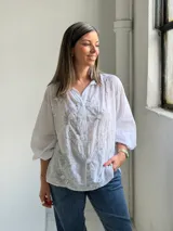 Camisa blanca de corte holgado y manga larga, con delicados bordados florales en tono gris claro en el frente.