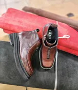 Botas cortas marca Lanka, confeccionadas en cuero vacuno color chocolate. Presentan una combinación de texturas, con paneles laterales de cuero grabado tipo reptil y frente liso. Cuentan con cierre frontal, puntera cuadrada y suela de plataforma dentada en color negro.