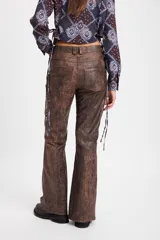 Pantalón de cuero color chocolate con efecto desgastado, de corte recto y tiro medio. Presenta costuras verticales en el frente y tajos laterales en el ruedo que aportan movimiento.