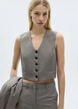 Chaleco de estilo sastre con diseño crop, cuello de pico y cierre frontal de botones. Presenta dos bolsillos de ribete en la parte delantera y cuenta con forro interior.