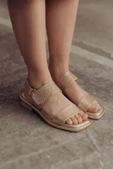 Sandalia Roma de cuero dorado, con tiras anchas, una lisa en la puntera y otra con textura reptil en el empeine, y tira ajustable al talón con hebilla. Suela plana y cómoda.