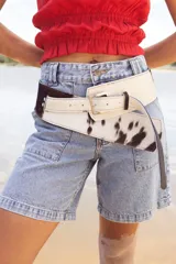 Cinto faja de cuero con estampado de vaca en blanco y negro, con hebilla metálica.