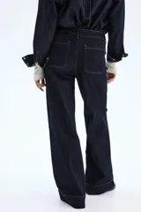 Pantalón de jean de tiro alto, color azul oscuro (índigo), con pierna ancha y corte cropped. Presenta bolsillos de parche grandes en la parte delantera y costuras en color ocre.