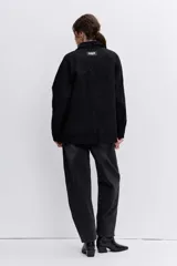 Campera de denim negro con cierre frontal y botones a presión, cuello clásico y bolsillos laterales.