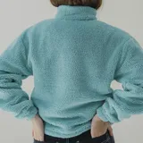 Buzo de sherpa color celeste con corte a la altura del pecho y bolsillo de nylon azul con logo estampado.
