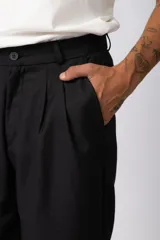 Pantalón sastrero de corte baggy, color beige, con pinzas frontales, cierre de botón y cremallera, y bolsillos laterales.
