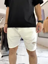 Bermuda deportiva tipo jogging color blanco, de corte recto con pequeño estampado lateral en marrón.
