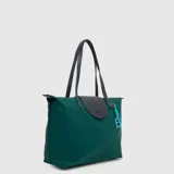 Bolso tipo tote color negro, de diseño minimalista y construcción impermeable. Cuenta con doble asa de hombro, solapa frontal con cierre magnético y detalle de logo grabado, y un charm colgante con la letra B en color fucsia.