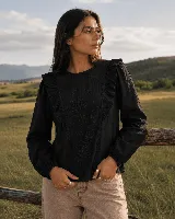 Blusa negra con bordado floral tono sobre tono y volados en el frente, de escote redondo y mangas largas con puños elásticos.