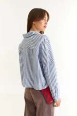 Camisa de corte holgado y diseño oversize, con estampado de rayas verticales en azul y blanco. Presenta cuello camisero, mangas largas con puños abotonados y costuras a contratono en color rojo.