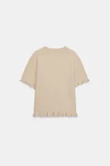 Jersey de punto de cuello redondo y manga corta, con detalle de volantes en el ruedo y en los puños.