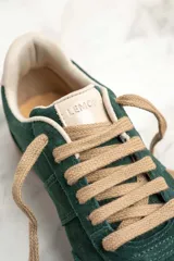 Zapatillas bajas color verde oscuro de gamuza con cordones color beige y suela de goma color marrón.