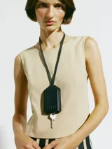 Llavero con funda de cuero negra en forma de casa, con correa para colgar al cuello. Incluye una llave plateada.