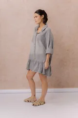 Vestido camisero corto de denim liviano azul con efecto desgastado, de corte oversize, con cuello camisero, botonadura frontal, bolsillo plaqué en el pecho, mangas largas y volado fruncido en el ruedo.