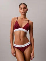 Bralette Calvin Klein de corte triangular, confeccionado en mezcla de algodón elástico y modal, con estampado gráfico en tonos rojos y banda elástica inferior en color blanco con el nombre de la marca en contraste.