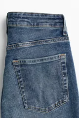 Jean de tiro alto con corte acampanado desde la rodilla, confeccionado en denim con leve elasticidad. Presenta diseño clásico de cinco bolsillos, cierre frontal con botón y acabado en tono azul medio.