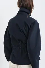 Parka de cuello alto con trabilla y manga larga, color azul marino. Presenta bolsillos laterales ocultos en la costura y cintura ajustable con cordón. El cierre frontal es con botones ocultos por solapa.