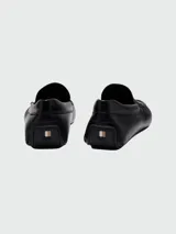 Mocasines de cuero negro con diseño clásico, costuras visibles en la puntera y detalle de logo grabado en el lateral.