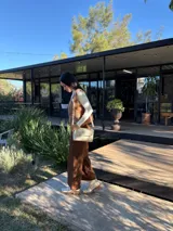 Cartera tipo bandolera de cuero color crudo, con diseño rectangular, solapa frontal con detalle de costura decorativa en el borde y correa ajustable.