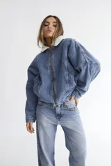 Campera bomber de denim azul oscuro con costuras a contratono en color verde. Presenta cuello de corderito en color marrón, cierre frontal y diseño holgado.