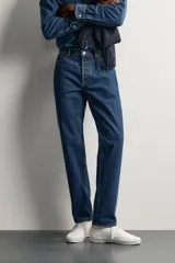 Jeans regular fit de tiro medio, confeccionados en denim de algodón azul oscuro con efecto lavado. Presenta diseño clásico de cinco bolsillos, pierna recta y cierre frontal con cremallera y botón.