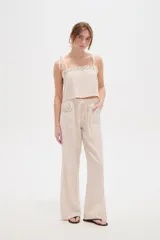 Pantalón ancho de viscosa color beige claro, de tiro alto con cintura elastizada y cordón ajustable. Presenta bolsillos laterales decorados con detalles bordados geométricos.