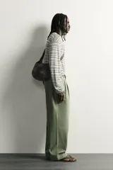 Pantalón chino baggy fit color verde militar, confeccionado en denim de algodón rígido, con corte holgado, tiro medio y pliegues frontales. Presenta bolsillos laterales y cierre frontal con cremallera y botón, con efecto lavado.