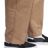 Pantalón Adidas de corte recto y estilo holgado, color beige. Presenta cintura elástica con cordón interno, bolsillos laterales con cierre y detalle de costura vertical frontal (pintuck) con el logo de la marca bordado en la pierna.