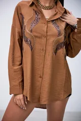 Camisa marrón de manga larga con detalles de lentejuelas y bordados en el frente. Tiene cuello clásico y botones frontales.