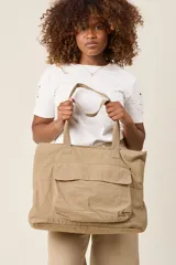 Bolso tote color beige, de tela tipo paracaídas, con doble asa de mano y bolsillo frontal con solapa.