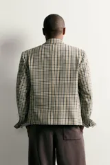 Blazer de corte boxy fit de Zara, confeccionado en tejido con algodón con estampado a cuadros en tonos beige, negro y blanco. Cuenta con cuello de solapas de muesca, manga larga con botones en los puños, bolsillos de vivo en el pecho y de plastrón en la cadera, y cierre frontal con un botón.