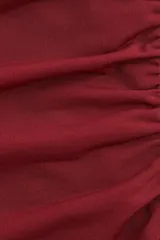 Top ajustado de punto color vino tinto, con escote bote, manga japonesa corta y fruncidos laterales que generan un efecto drapeado.