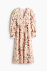 Vestido largo de mezcla de viscosa en color beige con estampado floreado. Presenta un escote en V pronunciado, botonadura frontal con botones forrados, y mangas largas abullonadas con puños ajustados. Cuenta con costuras fruncidas bajo el busto y en la cintura, dando paso a una falda de corte fluido y leve vuelo.