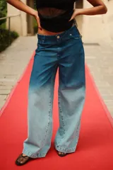 Jean de tiro medio con corte oversize y botamanga ancha. Presenta un diseño de lavado degradado que va de un azul intenso en la cintura a un tono claro en la parte inferior, con efecto gastado. Incluye avíos metálicos y badana de PU.