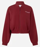 Campera deportiva tipo bomber de color bordó, con cierre frontal por cremallera, cuello redondo, mangas largas con puños elásticos y bolsillos laterales. Presenta un detalle de lettering bordado en el pecho.