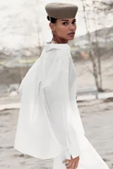 Blusa blanca confeccionada en lino, con cuello polo, escote en V y mangas largas amplias. Presenta un diseño holgado y bajo asimétrico.