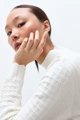 Sweater de punto color crudo con cuello alto tipo media polera, manga larga y diseño con textura de líneas horizontales. Presenta un borde inferior con terminación ondulada.