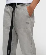 Pantalón de corte relajado, color gris claro lavado, confeccionado en algodón orgánico. Presenta cintura elástica con trabillas, cinturón negro ajustable con hebilla metálica, bolsillos laterales y el número 10 bordado.