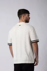 Camisa de punto de manga corta con cuello tipo bowling y cierre frontal de botones. Presenta un diseño texturizado con franjas verticales y detalles de contraste en blanco en los bordes de las mangas.